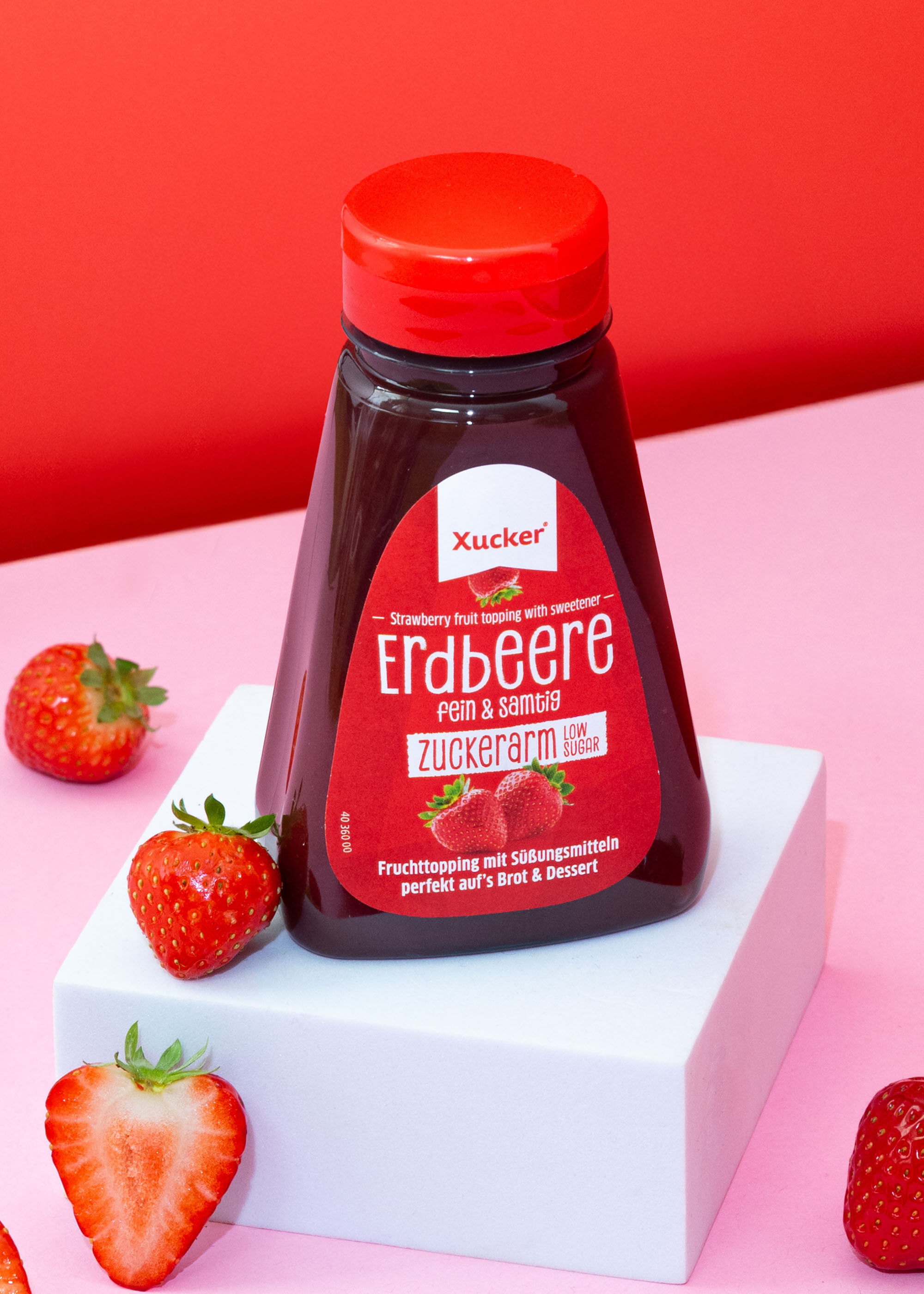 Flasche Xucker Erdbeer-Fruchttopping mit frischen Erdbeeren auf pinkem Hintergrund.