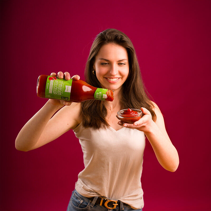 Junge Frau mit Flasche Ketchup ohne Zuckerzusatz und Schälchen in der Hand 
