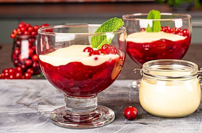 A bowl of vibrant Rote Grütze topped with fresh whipped cream and served with vanilla sauce